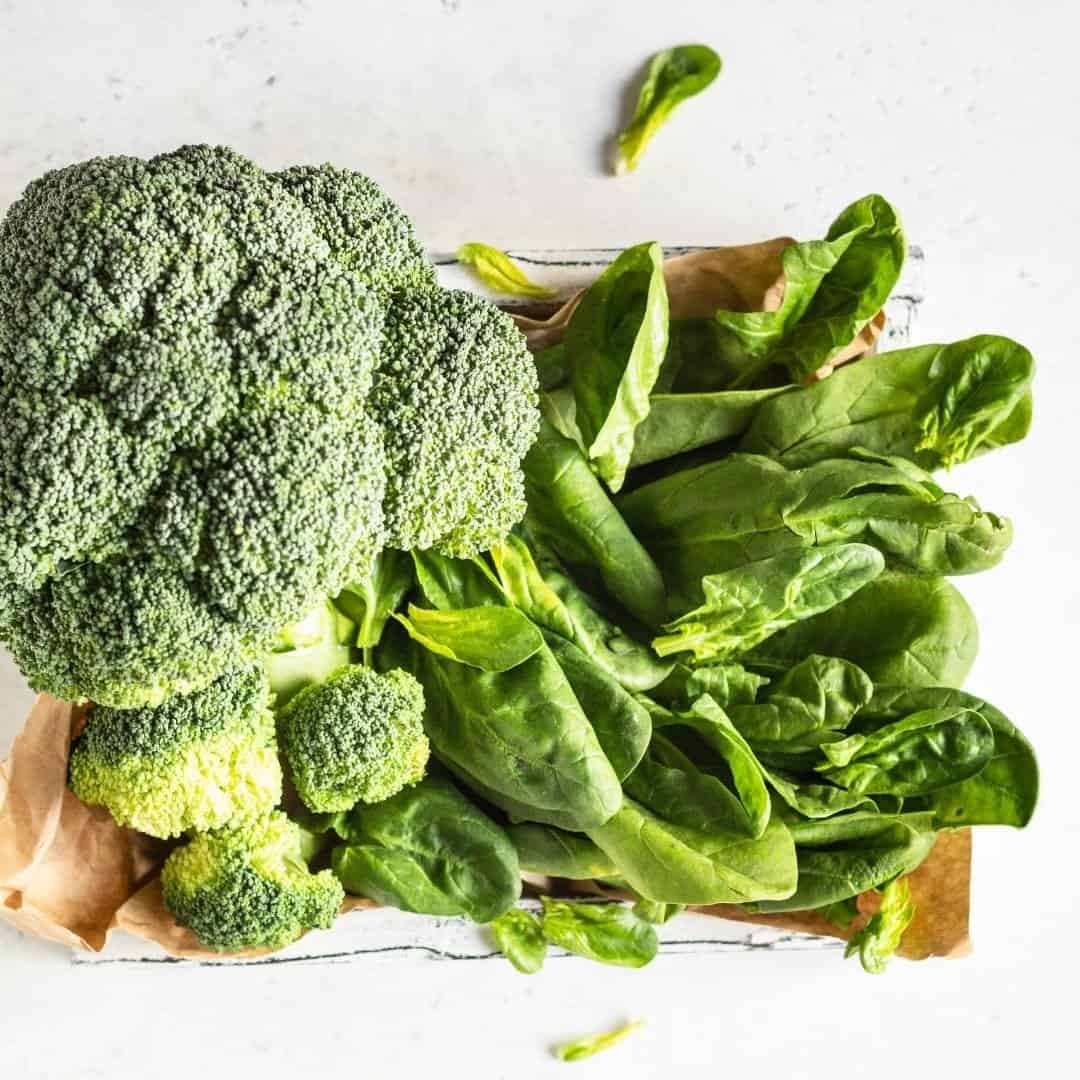 Broccoli and spinach, foods that balance blood sugar, on a white countertop.