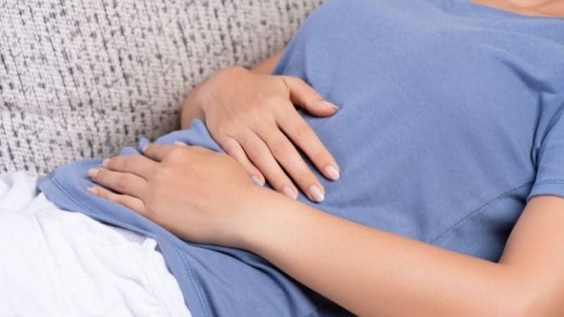 Woman holding stomach on couch common cause of bloat.
