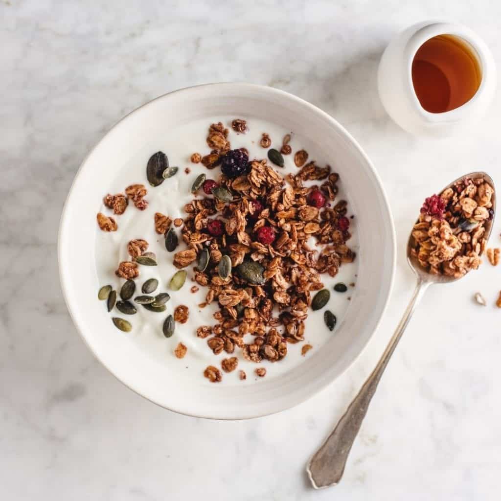 Homemade gluten-free granola in a white bowl with fresh berries and pumpkin seeds.