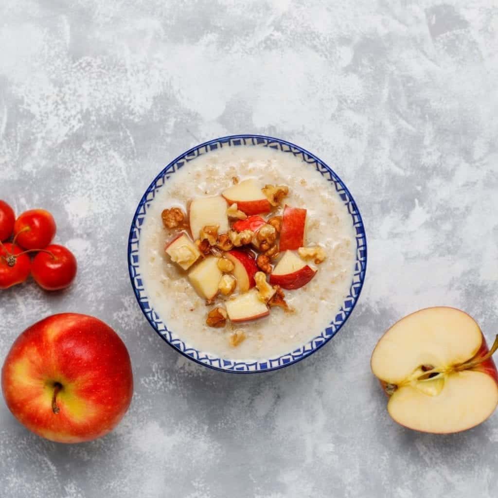 Healthy snack of oatmeal in a bowl with honey, red apple slices, and walnuts.