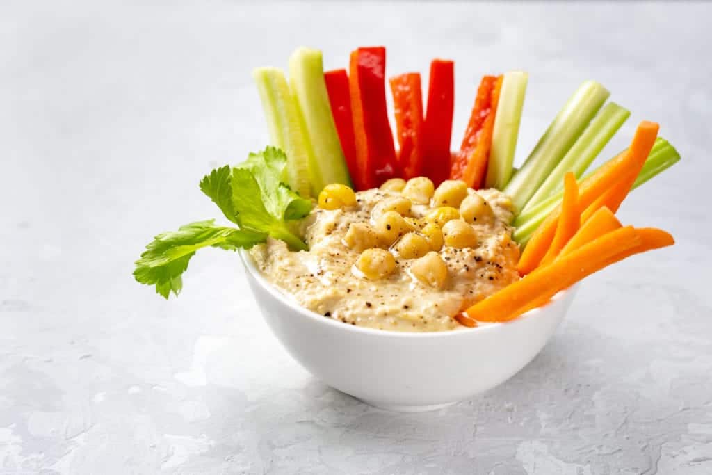 Delicious and healthy snack bowl with fresh hummus dip and cut vegetable sticks.