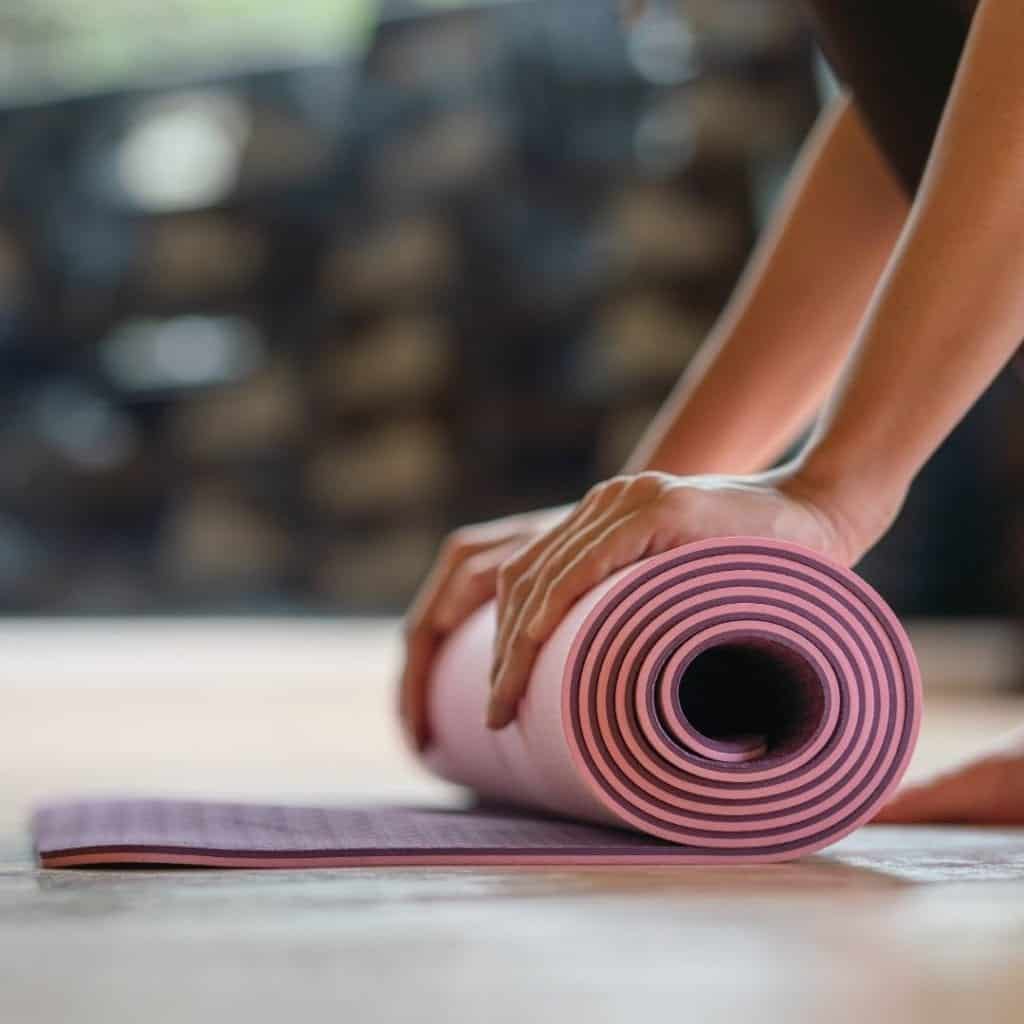 Woman rolling up a pink yoga mat after yoga meditation.