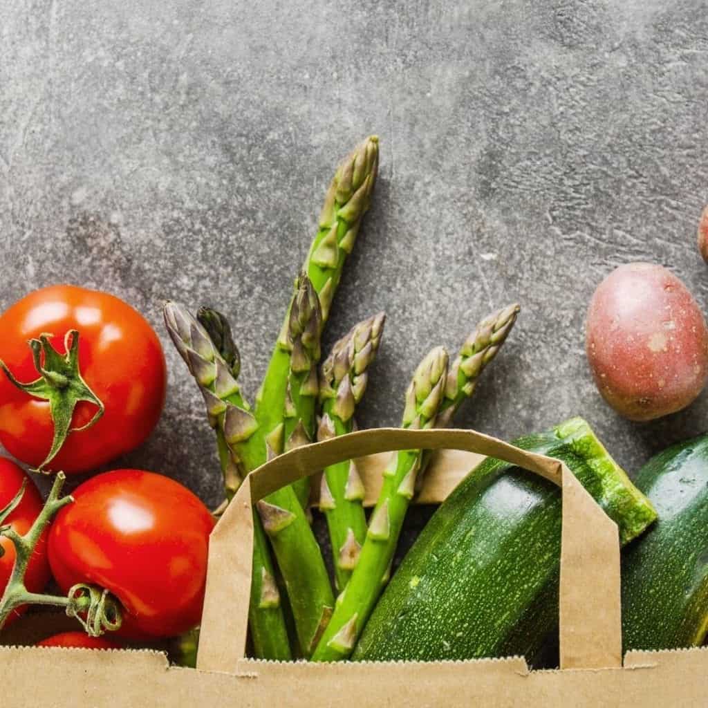 Tomatoes, asparagus, potatoes, and zucchini in a brown shopping bag, which is how to eat healthy on a budget and lose weight.