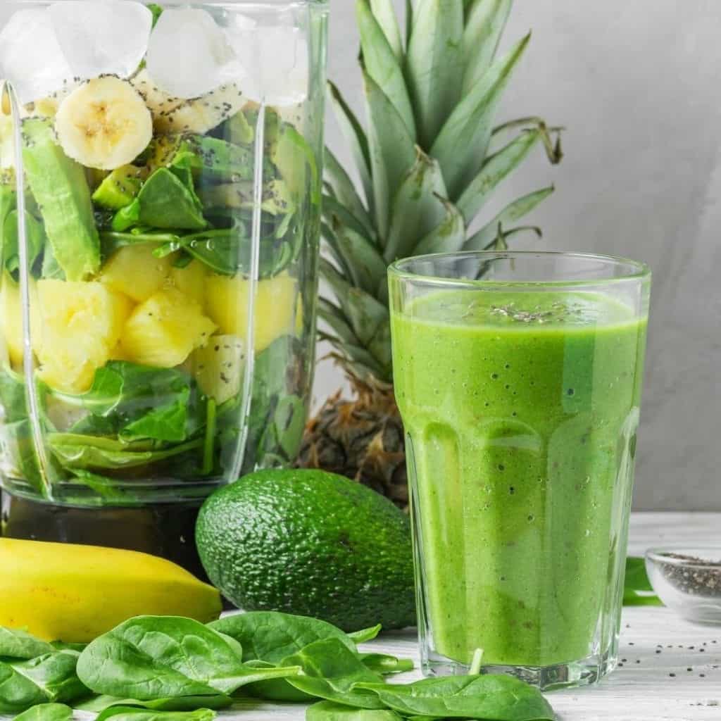 Natural energy boosting ingredients without caffeine, including a green smoothie on a table with avocado, spinach, banana, chia seeds, and pineapple