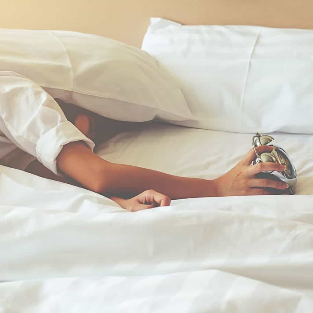 Woman in bed turning off alarm clock, one of 5 best tips on how to get the best sleep