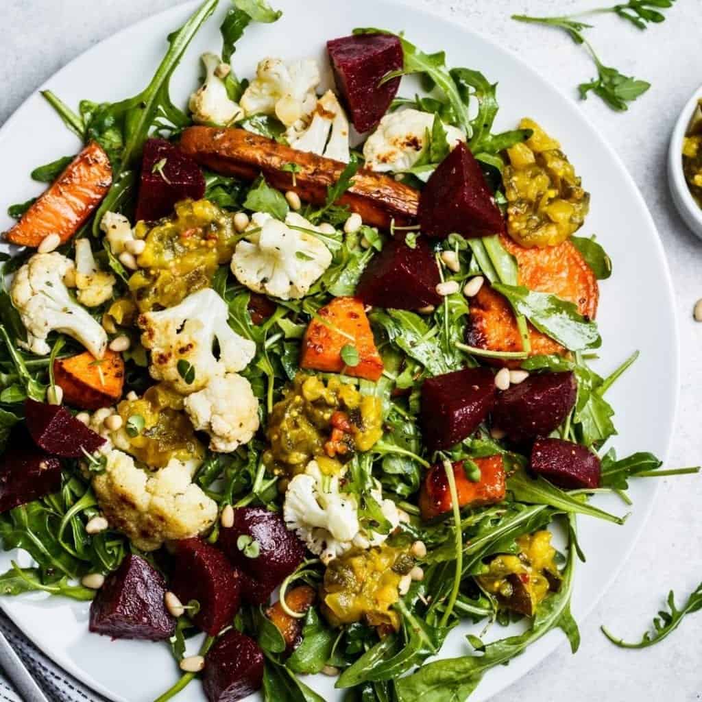 Start creating new habits by eating beet energy salad made with sweet potatoes, beets, cauliflower, apple, chickpeas, mixed greens, and pine nuts on a white plate.