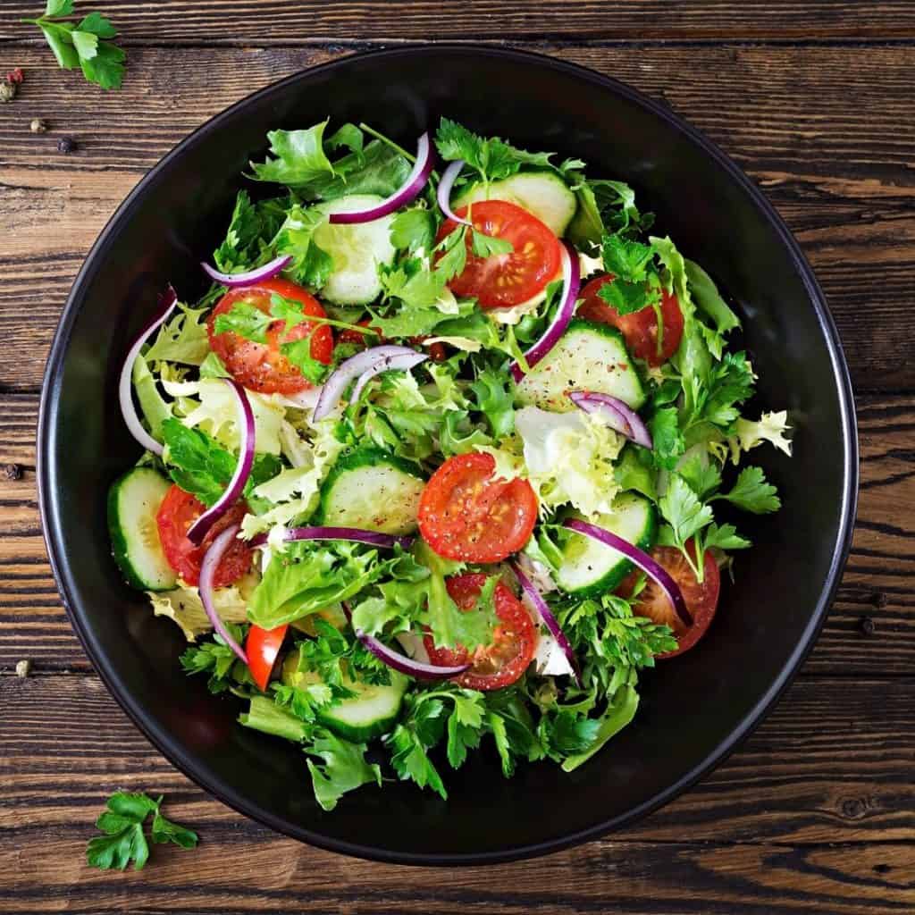 Salad in a black bowl filled with hydrating foods like cucumber, iceberg lettuce, and tomatoes. 