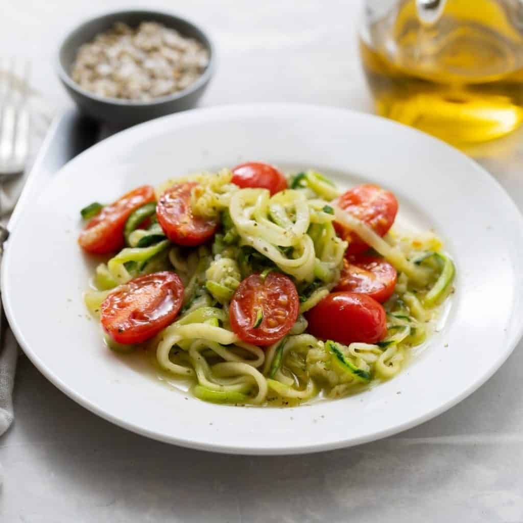 White plate of zoodles with fresh tomatoes and olive oil. 