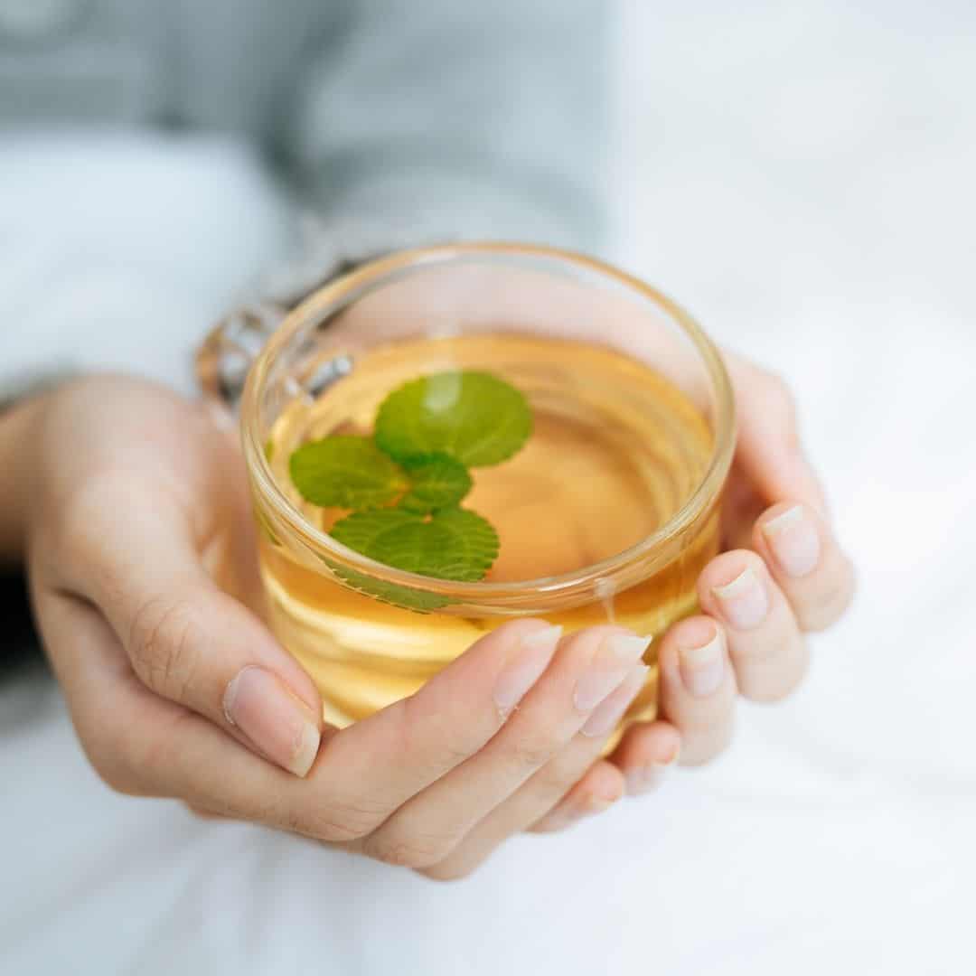 Woman holding a clear glass of green tea.