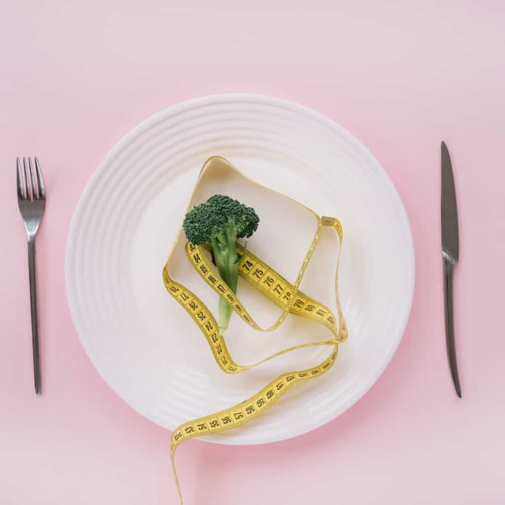 White plate with piece of broccoli and tape measure. There are simple ways to lose weight without dieting.