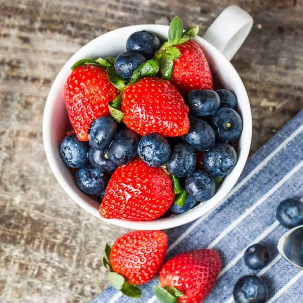 Fresh strawberries and blueberries in a white coffee mug.