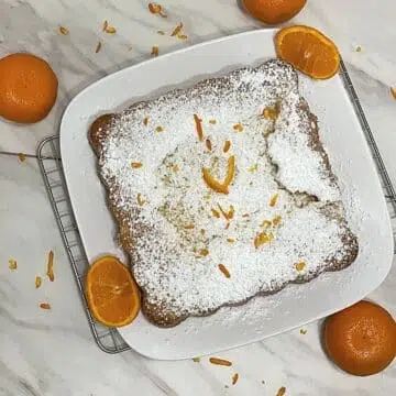 Healthy gluten free olive oil cake on a serving plate with oranges.