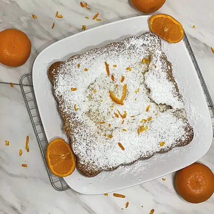 Healthy gluten-free olive oil cake on a serving plate with oranges.