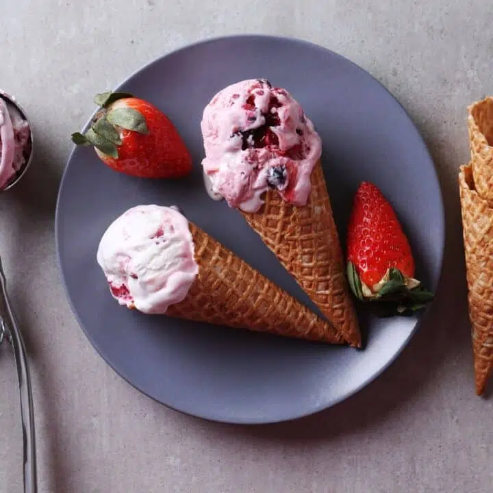 Vegan strawberry ice cream in a cone on a blue plate with fresh strawberries.